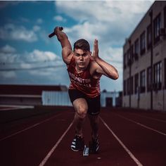 a man in red shirt and black shorts running on a track with his hands up