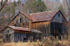 an old wooden barn in the woods with rusted metal roof and tining on it