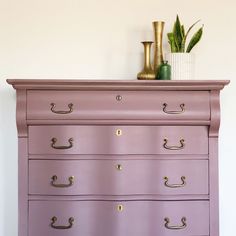 a pink dresser with gold handles and brass knobs on the bottom drawer, in front of a white wall