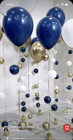 blue, white and gold balloons are hanging from the ceiling in a room with marble flooring