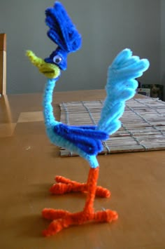 a blue and orange bird made out of yarn sitting on top of a wooden table