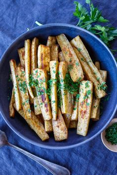 french fries with parsley in a blue bowl on a blue cloth next to a spoon