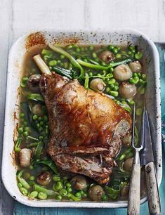 a roasting pan filled with meat and vegetables next to a knife, fork and spoon