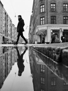 black and white photograph of man walking on street with buildings in the backgroud