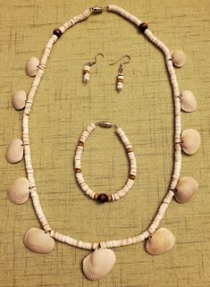 This is a jewelry set consisting of a necklace, bracelet, and earrings. Tiger conus heishi makes up the foundation of the jewelry. The necklace has eleven incongruous ark clam shells, which are native to the Gulf of Mexico. Wooden beads also highlight all of the pieces to complete the natural look. The necklace and bracelet are strung with nylon-coated stainless steel and have silver tone clasps. The earrings are made using silver tone eyepins and French hooks. The necklace measures 23 inches, the necklace measures 7 1/4 inches, and the earrings measure 1 5/8 inches from top of hook to bottom of eyepin. Hand-strung Shell Jewelry As Gift, Hand-strung Shell Jewelry For Gifts, Clam Shells, Bracelet And Earring Set, Necklace And Bracelet, Shell Necklace, Gulf Of Mexico, Shell Necklaces, Lebanon