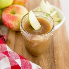 an apple cider is sitting on a cutting board next to apples and a plaid napkin