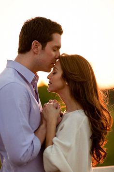 a man and woman standing next to each other in front of the sun at sunset