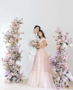 a man and woman standing next to each other in front of floral archways with pink flowers