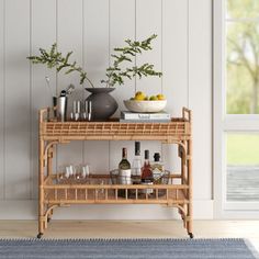 a bamboo bar cart with wine glasses and bottles on it in front of a window