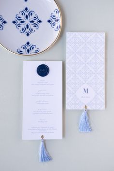 an elegant blue and white wedding stationery with tassels is displayed on a plate