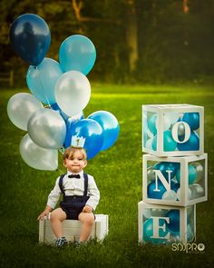 a little boy sitting on top of a box with balloons in the air and letters spelling out