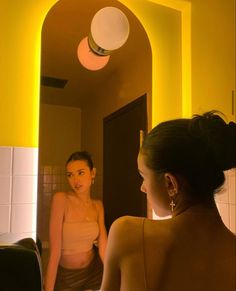 a woman standing in front of a bathroom mirror looking at her own reflection on the wall