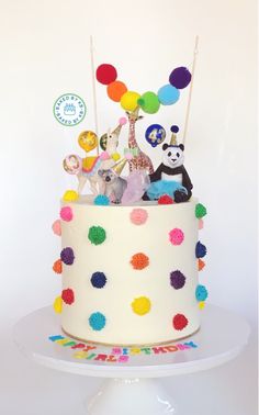 a birthday cake decorated with colorful pom poms and animals is on a white plate