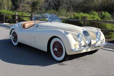 an old white car is parked on the side of the road in front of a wooden fence