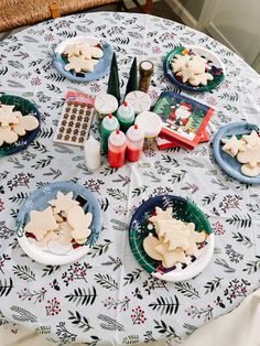 a table topped with plates and cookies on top of a white table cloth covered in snowflakes