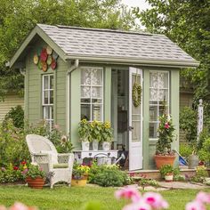 a garden shed with potted plants and flowers in the front yard, next to a lawn chair