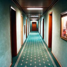 a long hallway with green walls and blue carpeted flooring, framed pictures on the wall