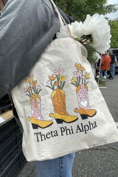 a person holding a bag that says thea phi alpha with boots and flowers on it