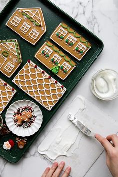 someone is decorating gingerbread houses with icing and sprinkles on a tray