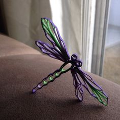 a purple and green dragonfly sculpture sitting on top of a brown couch next to a window