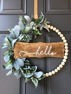 a wooden sign that says hello hanging on the front door with greenery around it