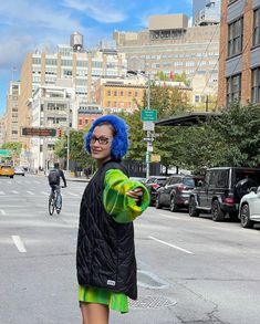 a woman with blue hair is standing on the street