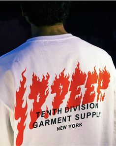 the back of a man wearing a white shirt with red flames on it that says, tenth division garment supply new york