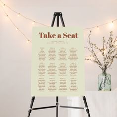 an easel with a seating chart on it in front of a string of lights