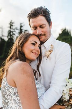 a man and woman hugging each other in front of the camera with trees in the background