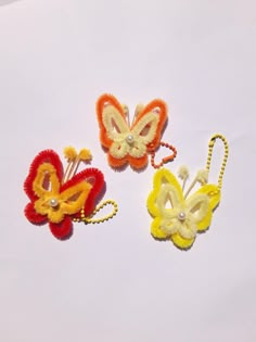 three different colored butterfly hair clips on a white surface with one yellow, one red and one orange