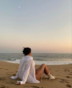 a woman sitting on top of a sandy beach next to the ocean