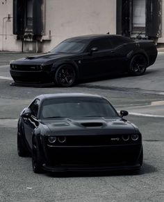 two black sports cars parked in front of each other on the street next to a building