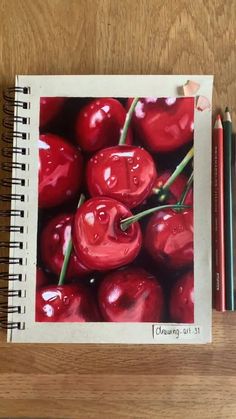 a drawing of cherries with two pencils next to it on a wooden table