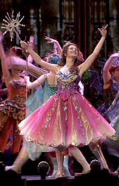 a woman in a pink and gold dress is dancing with other people on stage behind her