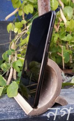 a cell phone sitting on top of a wooden stand in front of some green plants