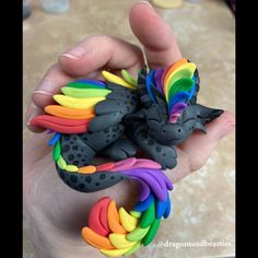 a hand holding a small toy dragon with rainbow colors on it's body and wings