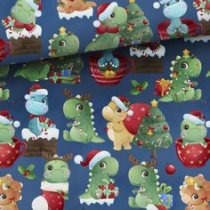 a blue christmas wrapping paper with green and red dinosaurs in santa hats on it, surrounded by other holiday themed items