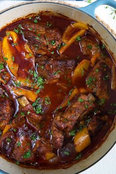 a pot filled with meat and vegetables on top of a blue table cloth next to bread