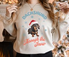 a woman wearing a dachshund through the snow christmas sweater in front of a tree