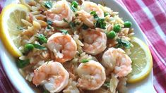 a white plate topped with pasta and shrimp next to lemon wedges on a table