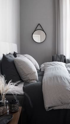 a bed with black and white striped sheets in front of a round mirror on the wall