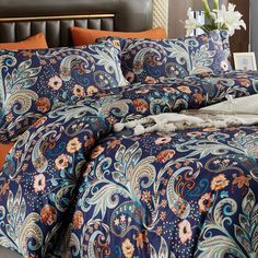 a bed with blue and orange comforters on top of it next to a night stand