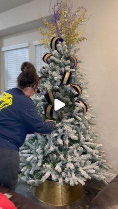 a woman decorating a white christmas tree with gold and purple ribbons on it's top