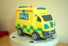 a cake shaped like a yellow ambulance on top of a white table with a red chair in the background