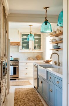 a kitchen with blue and white cabinets, an area rug and two pendant lights hanging from the ceiling