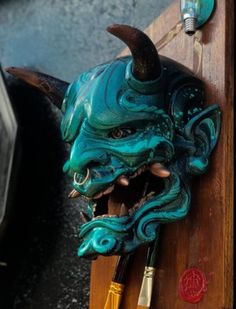 a green mask hanging on the side of a wooden wall next to paintbrushes