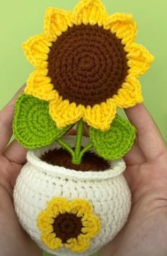 a crocheted sunflower sitting in a white pot with green leaves and brown bottom