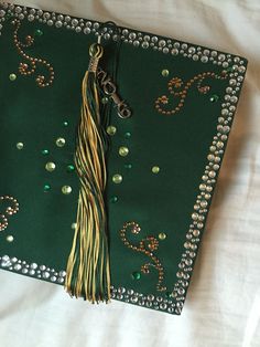 a green graduation cap with gold tassels and beads on the front, sitting on a white sheet