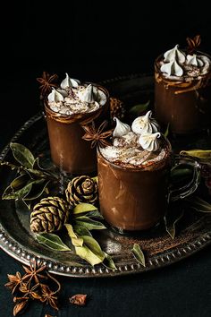 three desserts with whipped cream and cinnamon on a tray next to an evergreen cone