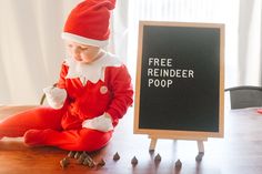 a little boy dressed as santa clause sitting in front of a sign that says free reindeer poop